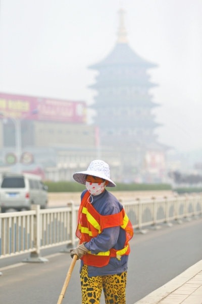 近日，在古都洛陽，環(huán)衛(wèi)工人身后的“天堂”被霧霾籠罩著。