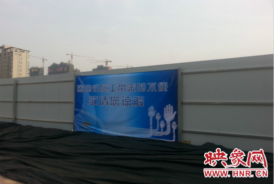 道路南側(cè)圍起了白色的圍擋，墻上標(biāo)示著“因地鐵施工帶來的不便敬請(qǐng)您諒解”的提示牌。