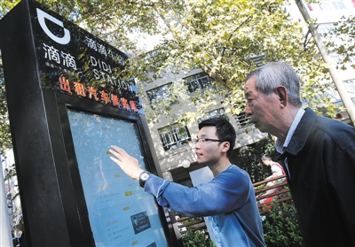10月15日，滴滴工作人員（左）指導乘客使用“滴滴車站”的電子屏預約出租車。