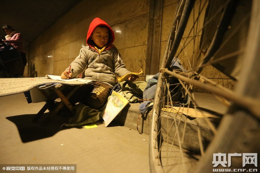 2015年11月8日晚，鄭州，7歲男孩涵洞橋下陪父母練攤，路邊燈下坐小馬扎上寫作業(yè)。