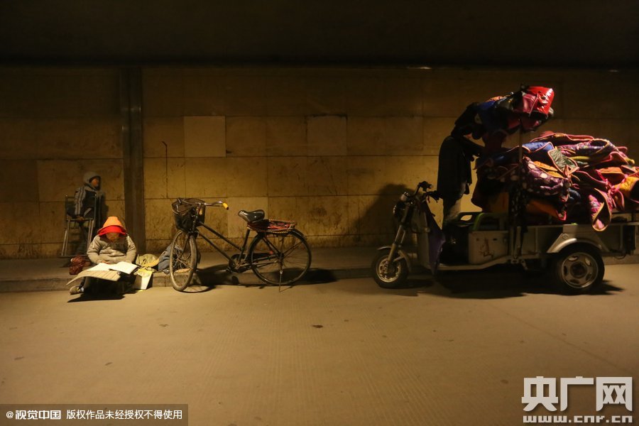 2015年11月8日晚，鄭州，7歲男孩涵洞橋下陪父母練攤，路邊燈下坐小馬扎上寫作業(yè)。