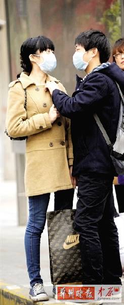 公交站臺(tái)上，一對(duì)年輕人戴著口罩，系緊衣領(lǐng)。